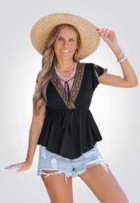 Zwarte peplumtop met geborduurde V-halsdetail, franjes, korte mouwen, gecombineerd met versleten denim shorts en een strohoed.