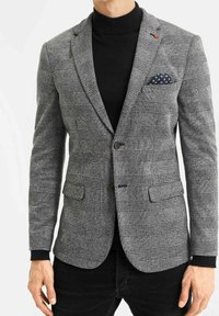 Grå rutig kavaj med texturerad tyg, slag och två knappar, samt framlommer. Bärs över en svart polotröja. Ficknäsduk ingår.