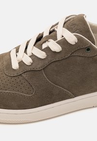 Olivengrønn semsket sneakers med perforerte detaljer, kremfargede snøringer og hvit gummisåle. Har sydd detaljer og en sirkulær malje.