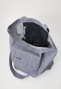 Torba tote z materiału w poziome paski w kolorze granatowym i białym. Wnętrze wykończone jednolitym czarnym podszewką, z kieszonką na zamek i przednią kieszonką z logo.