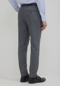 Pantaloni grigi con una texture liscia, passanti per cintura e una tasca posteriore con bottone. Indossati con scarpe nere e una camicia a righe visibile in cima.