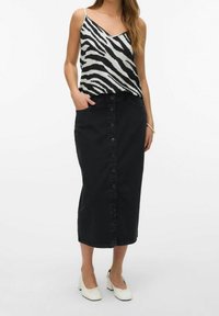 Falda de mezclilla negra con botones delanteros, combinada con una camisola de estampado de cebra en blanco y negro. Presenta tirantes ajustables y un corte relajado.