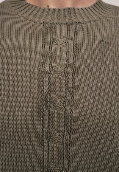 Nahaufnahme eines gestrickten taupefarbenen Pullovers mit zentralem Zopfmuster und geripptem Rundhalsausschnitt, der oberen Brust- und Halsbereich zeigt.