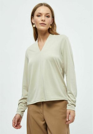 Licht beige lange mouwen top met een v-hals, gemaakt van gladde stof, met een ontspannen pasvorm en subtiele naaddetails. Gecombineerd met bruine broeken.