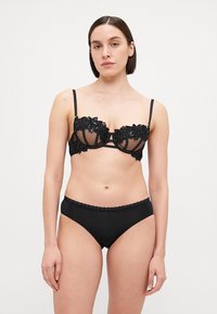 Schwarzes Dessous-Set mit einem durchsichtigen BH mit floralen Spitze-Details und verstellbaren Trägern, kombiniert mit glatten, hochtaillierten Slips.