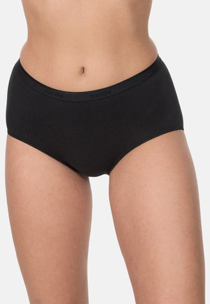 Kvinde iført sorte bomuldsunderbukser med høj talje, vist fra maven til øvre lår mod en ensfarvet baggrund.