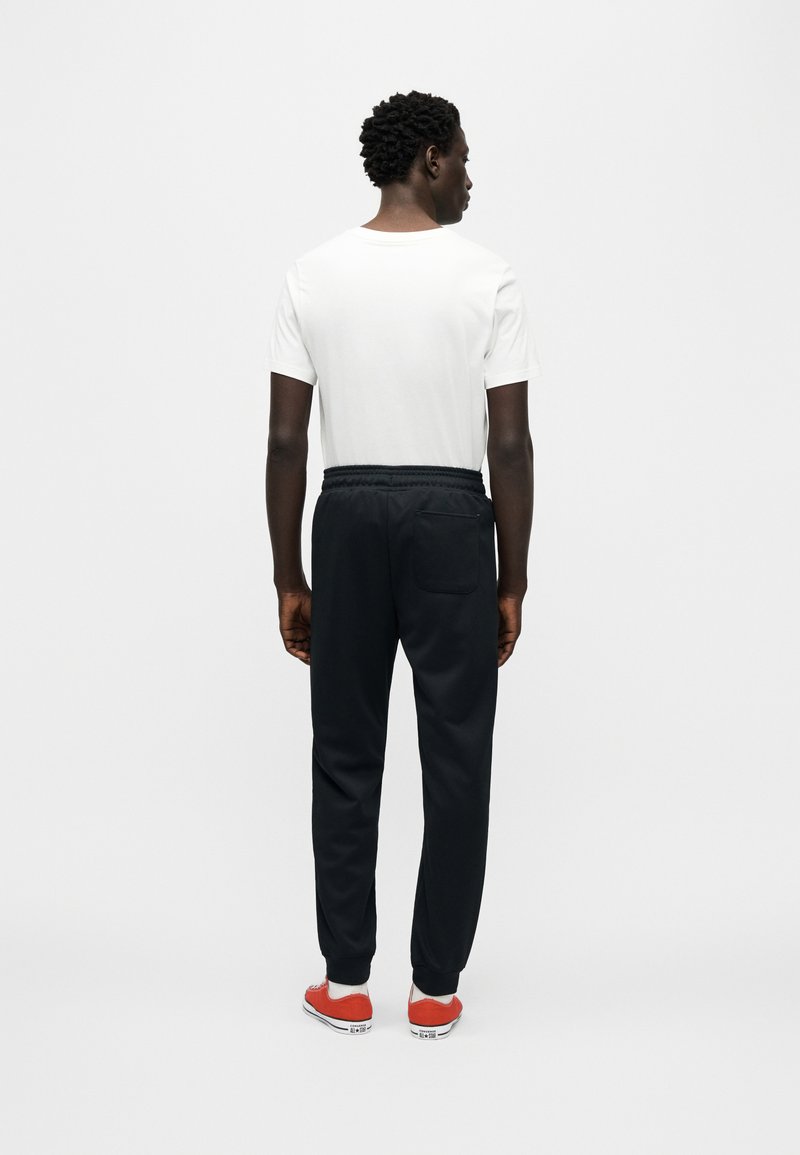 Hvid t-shirt med korte ærmer, sorte joggingbukser med elastik i taljen og røde sneakers med hvide såler. Enkel design, ingen synlige mønstre eller logoer.