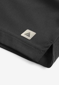 Article en tissu noir avec une texture lisse. Présente un logo triangulaire argenté sur une patte carrée. Les bords sont cousus avec un détail perforé.