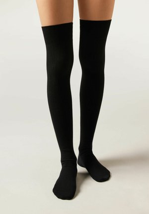 Schwarze, hüfthohe Socken aus geripptem Material. Glatte Textur, die über das Knie reicht, mit einem enganliegenden Design und runder Zehe.