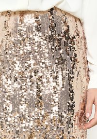 Pailletėta sijonas, kuriame dera auksinės ir rožinės aukso atspalviai, su lygiu paviršiumi ir blizgančiomis apvalių paillette, išdėstytomis vertikaliai.