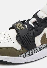 Nike sportcipő, fehér bőr felsőrésszel, zöld és fekete részletekkel, textúrázott oldalsó panelek, perforációk és fekete tépőzáras pánt.