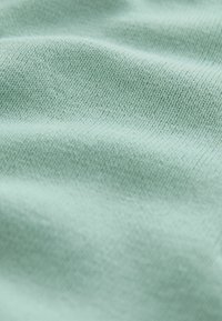 Gros plan sur un tissu tricoté doux de couleur vert clair, montrant une texture détaillée et des coutures fines avec de légers plis.