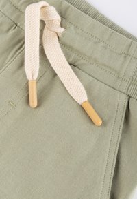 Olive green shorts featuring a soft, textured fabric, with a woven beige drawstring and wooden tips. Close-up of waistband detailing.