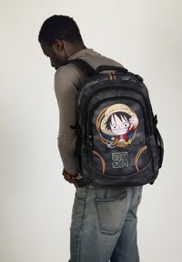 Mochila negra con un diseño de personaje de dibujos animados, que presenta a Luffy de One Piece, y acentos a rayas. Tela texturizada con múltiples bolsillos.