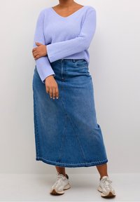 Pull en tricot violet clair à manches longues, associé à une jupe en denim bleu mi-longue avec un détail de couture à l'avant, et des baskets blanches.