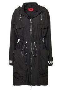 Giacca nera con cappuccio, coulisse in vita, cerniera frontale, due tasche sul petto e grandi tasche laterali. Presenta dettagli con il logo sulle maniche.