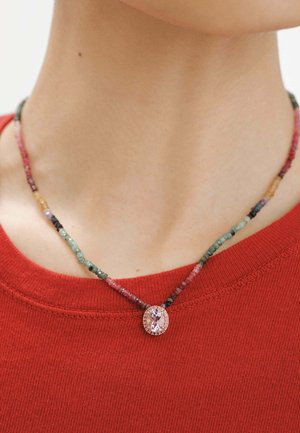 Collar de cuentas multicolores con un colgante ovalado de gema rosa, que presenta un acabado metálico, llevado sobre una camiseta roja.