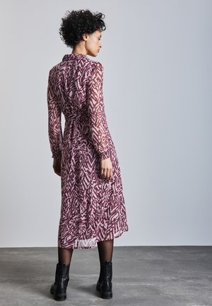 Robe longue et transparente couleur mauve avec un motif abstrait, taille cintrée et manches longues. Assortie avec des bottines noires et des collants transparents.