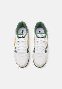Sneakers bianche con accenti verdi e gialli, realizzati in materiali mesh e camoscio, punta rotonda e lacci piatti. Logo Diadora sulla linguetta.
