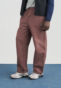 Nike laisvalaikio kelnės švelnios bordo spalvos, su elastine juosmens juosta, šoninėmis kišenėmis ir subtiliu logotipu. Derinamos su pilkomis Nike sportinėmis avalynėmis.