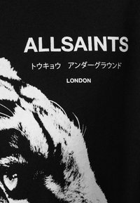T-shirt nera in cotone con una grafica di una tigre bianca e il testo audace "ALLSAINTS", con testo aggiuntivo in giapponese e "LONDON" sottostante.