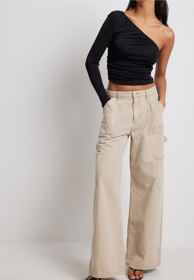 Svart one-shoulder topp med rynkad textur, i kombination med beige vida cargobyxor med sidofickor och avslappnad passform.