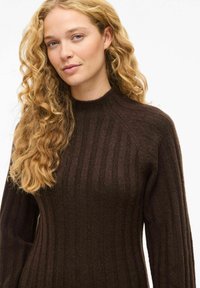 Pull en tricot côtelé marron avec un col montant et des manches longues, présentant des rayures verticales et une finition texturée.