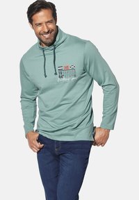 Light teal pullover hoodie featuring a high collar, black drawstrings, and graphic print with flag icons. Made from a soft fabric.