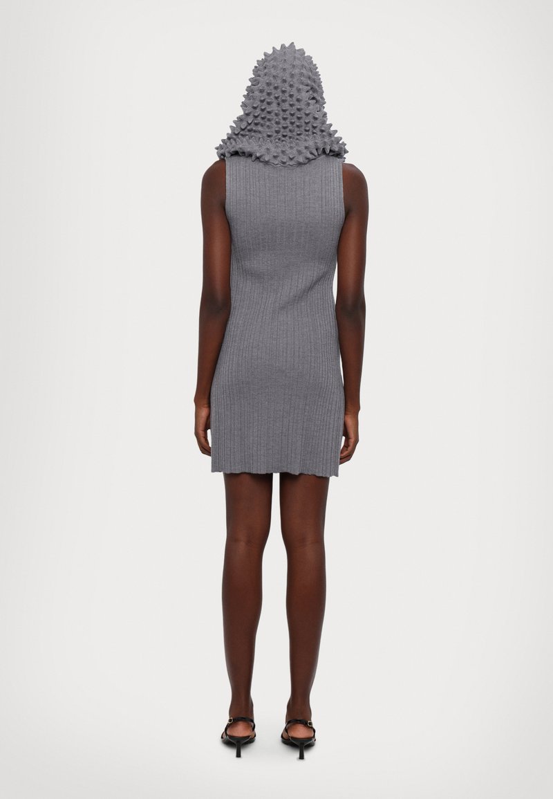 Abito grigio a coste con cappuccio testurizzato e a punte. L'abito è aderente con un orlo leggermente scalloppato, abbinato a scarpe con tacco nere e cinturini.