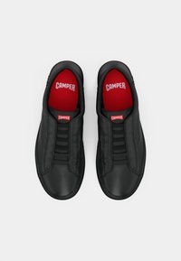 Schwarze Slipper aus glattem Leder mit elastischen Riemen und roten Innensohlen mit "CAMPER"-Markenlogo. Schlichtes, abgerundetes Design.