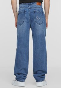 Jeans in denim blu con una vestibilità comoda, caratterizzati da una patch in pelle sul retro e una firma ricamata in bianco sulla tasca destra.