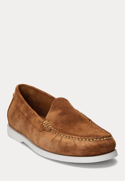 Mocassin à enfiler en daim marron avec couture beige et semelle en caoutchouc blanche, présenté en angle pour montrer les détails latéraux et avant.