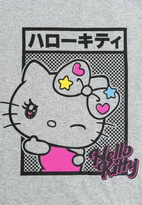 T-shirt grigia con un contorno nero di Hello Kitty, un fiocco colorato, dettagli rosa e testo giapponese sopra in un riquadro.
