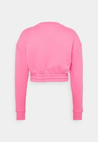 Felpa accorciata di un brillante colore rosa. Presenta maniche lunghe, polsini a coste e orlo arricciato per un look aderente. Texture morbida, design casual.