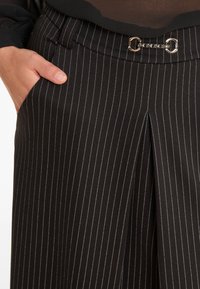 Schwarze Nadelstreifenhose aus einem glatten Stoff, ausgestattet mit einer Fronttasche und einem silbernen Kettendetail am Bund.