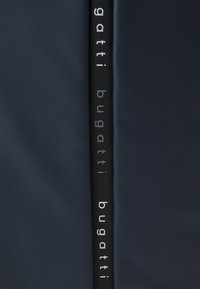 Sinih olematud kott, millel on sile tekstuur, vertikaalne must rihm, millel on valgest kirjatüübis "gatti" ja "bugatti".