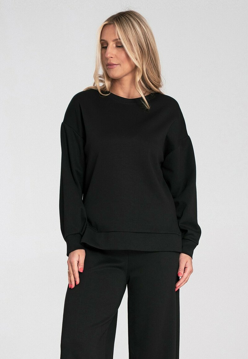 Czarna bluza wykonana z miękkiego materiału, z okrągłym dekoltem, opuszczonymi ramionami i luźnym krojem, zestawiona z pasującymi spodniami typu wide-leg.