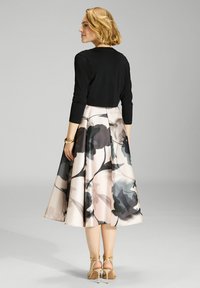 Suéter negro cortado sobre una falda floral rosa con acentos en verde oscuro y gris; tejido suave y forma acampanada; tacones dorados con tiras.