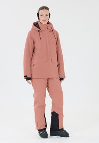 Veste de ski imperméable rose avec capuche, fermeture éclair à l'avant et poches, associée à un pantalon assorti avec des accents noirs et une texture lisse.