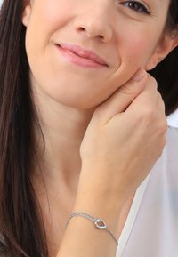 Zilveren armband met een hartvormige sluiting, voorzien van een delicate ketting en een gladde afwerking, gedragen om een pols met een lichte huidtint.