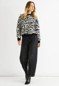 Schwarzer und weißer gemusterter Pullover mit einem Leoparden- und Zebra-Design, mit einem gerippten schwarzen Saum und Bündchen, kombiniert mit locker sitzenden schwarzen Jeans.