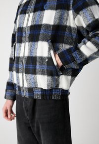 Fuzzy, black and white plaid jacket with blue accents, zip closure, long sleeves, and side pockets; textured fabric, contrasting colors.