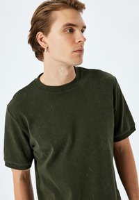 Olivgrön t-shirt i mjuk bomull med rund hals och korta ärmar, med en lätt blekt textur och minimalistisk design.