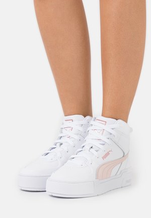 Białe wysokie sneakersy marki Puma z różowym logo i wzorem, noszone na stopach osoby na jednolitym białym tle.