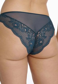 Turkusowe koronkowe majtki z falbanym brzegiem i floralnym wzorem. Przezroczysta tkanina podkreśla złożoną koronkową detale w talii.