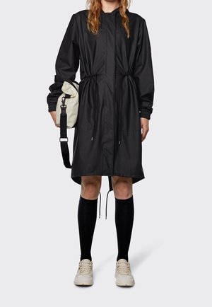 Černý voděodolný kabát s nastavovací šňůrkou v pase, elastickými manžetami a dvěma bočními kapsami. V kombinaci s podkolenkami a lehkými teniskami.