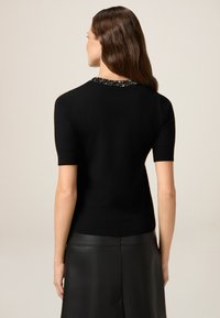 Haut en tricot noir à manches courtes avec un col en perles. Le tissu est lisse, avec une silhouette ajustée et un ourlet côtelé.