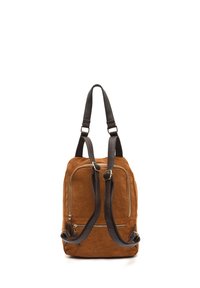 Sac à dos en suède marron avec des sangles en cuir noir. Il possède deux poches zippées à l'avant et une texture lisse, conçu pour un usage casual.