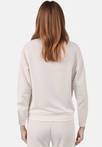 Licht beige sweatshirt met een eenvoudig ontwerp, lange mouwen, ribbels bij de manchetten en onderkant. Glad textuur. Zicht van achteren.