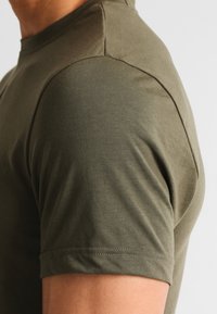Olive green cotton t-shirt featuring a crew neck, short sleeves, and smooth texture, with visible stitching details on the shoulder.